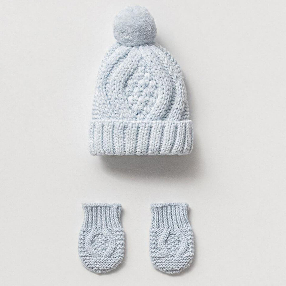 Knitted baby hat with pom-pom and matching mittens on a light gray background